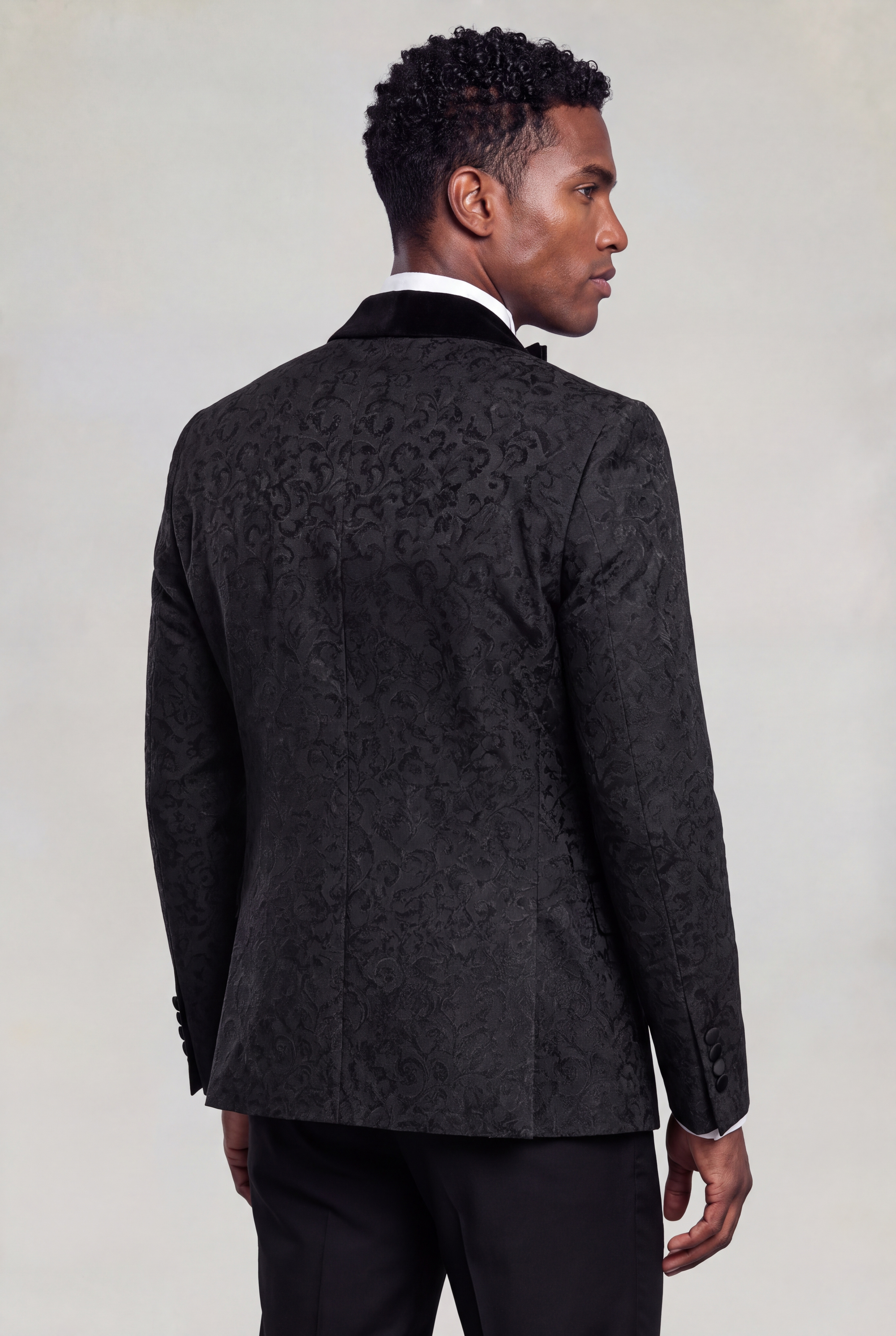 Rear three-quarter view showing the subtle damask pattern and tailored shape of a black tuxedo jacket from Gentleman's Guru