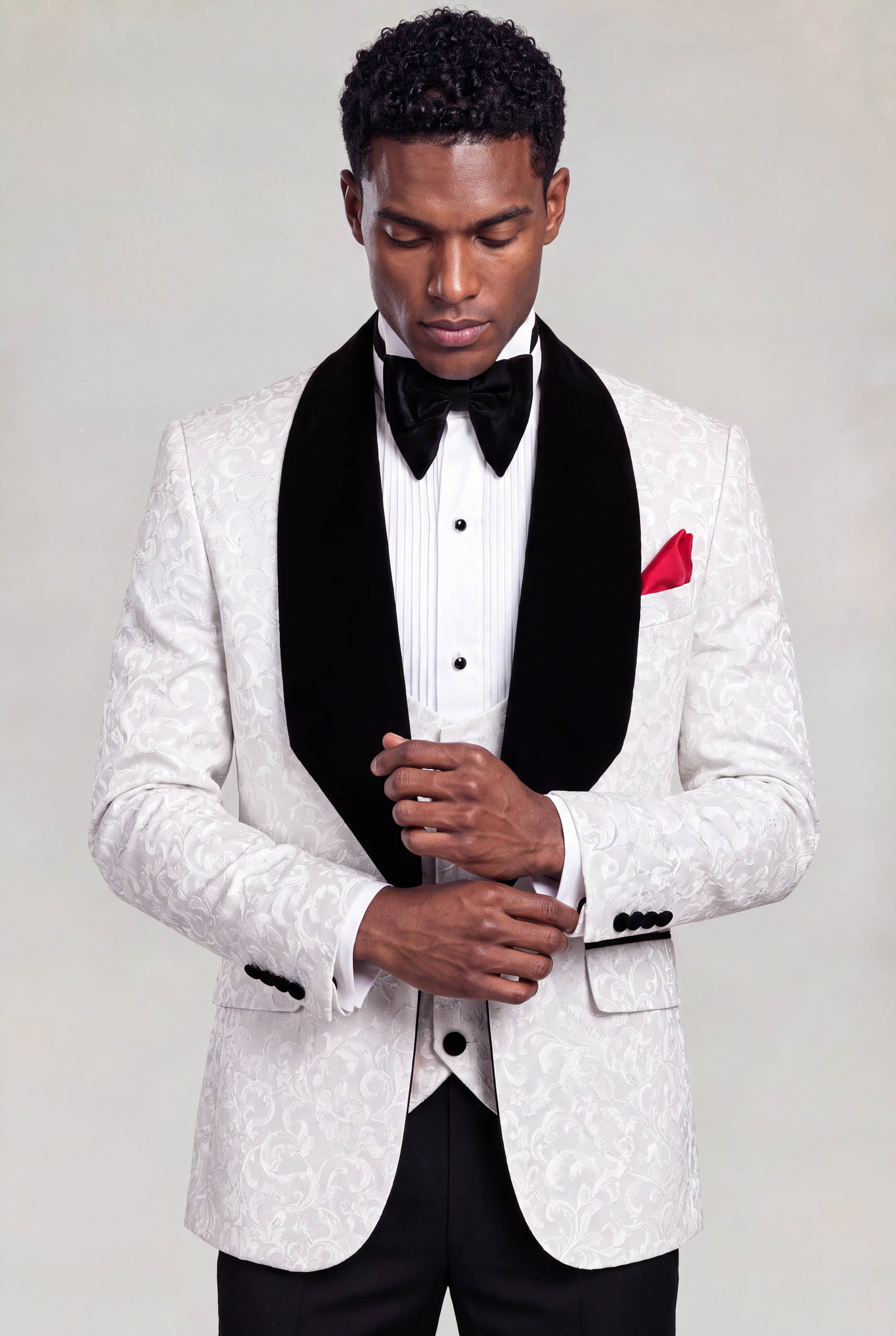 Model adjusting his cuff in a white floral tuxedo with black velvet shawl lapels from Gentleman's Guru
