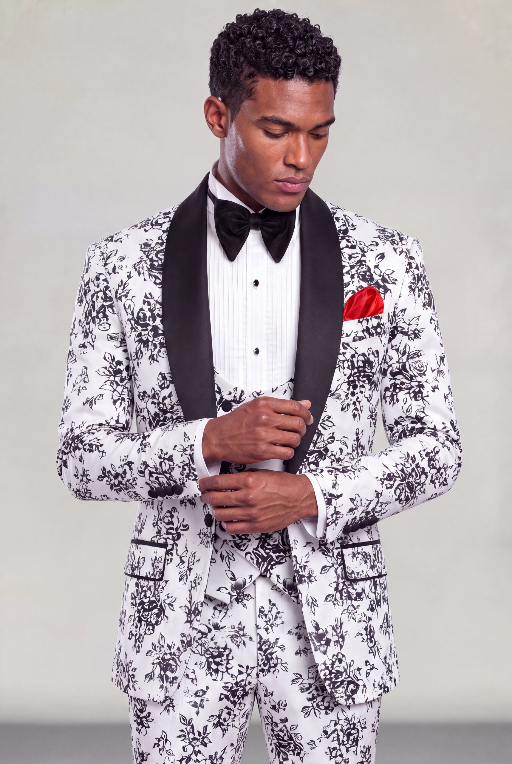 Model adjusting the cuff of a floral tuxedo with black satin shawl lapels and matching vest from Gentleman's Guru