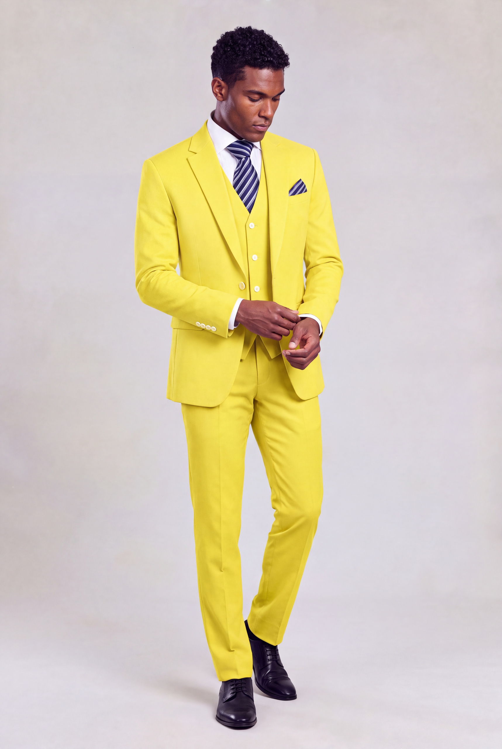 Full-length view of a man adjusting his cuff in a pastel yellow suit with matching trousers and black dress shoes from Gentleman's Guru