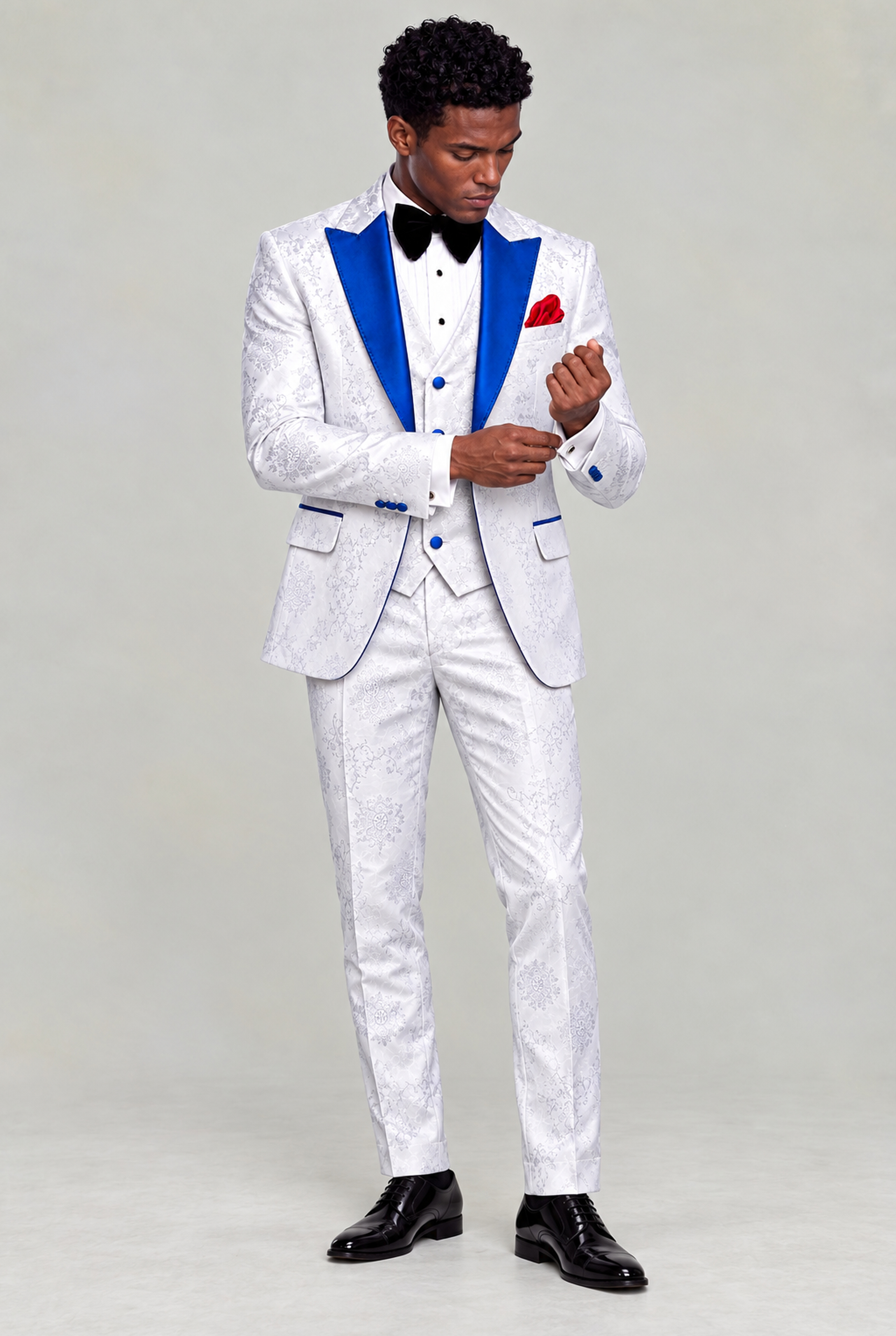 Full-body view of a model looking down and adjusting his cuff in the white floral suit with blue lapels from Gentleman's Guru