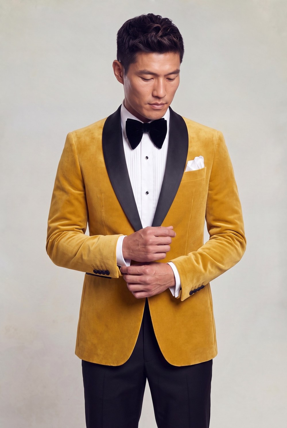 Asian male model adjusting his cuff in a gold velvet tuxedo jacket with black shawl lapels