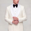 Model adjusting his cuff in a closed cream patterned tuxedo with broad white satin shawl lapels from Gentleman’s Guru