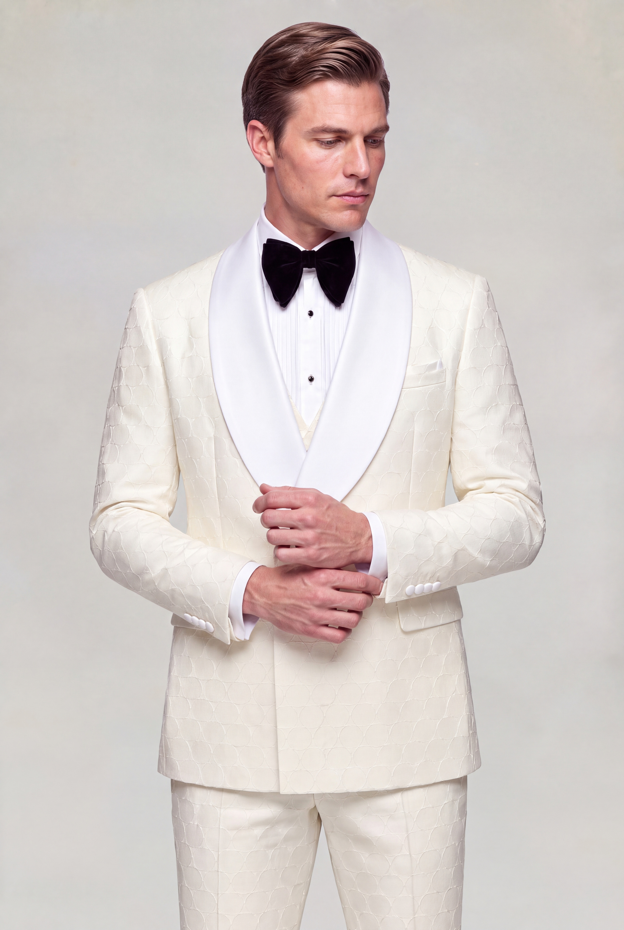 Model adjusting his cuff in a closed cream patterned tuxedo with broad white satin shawl lapels from Gentleman’s Guru