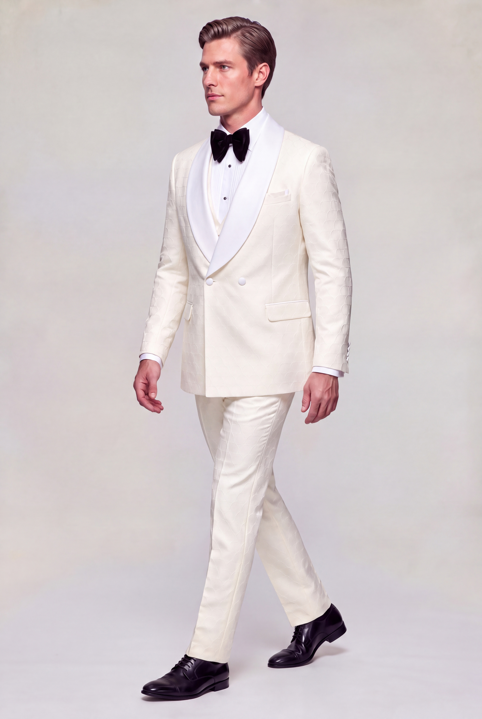 Side walking view of a closed double breasted cream tuxedo with matching patterned pants and black dress shoes from Gentleman’s Guru